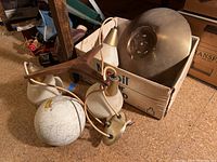 Overall view of three hanging light fixtures on floor with wood frame and frosted glass shades, one shade visibly broken, showing condition and contents of the lot.