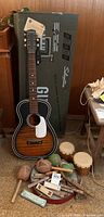 Full view of guitar standing next to its original Sears Silvertone box with percussion instruments arranged in front on the floor.
