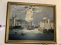 Front view of oil painting showing ships docked at pier with buildings and cloudy sky, inside gold frame.