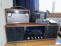 Zenith Deluxe Royal 755 atop Lafayette tabletop radio with a small black device beside Sanyo portable radio.