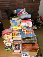 Full view of vintage Red Sox bobblehead in front with multiple playing card decks and board games stacked behind it, Bob Feller baseball card visible
