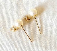 Pair of small stud earrings with a natural pearl and clear crystal stone, 10K gold posts, displayed on white fabric.