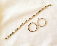 Sterling silver bracelet laid flat beside pair of hammered hoop earrings on white fabric background.