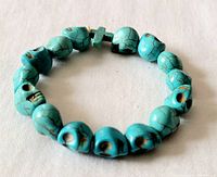 Turquoise skull beads stretch bracelet arranged in circle, showing detail on gemstones and cross bead.