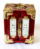 Front view of vintage Chinese jewelry box showing red lacquered wood, brass fittings, and carved stone details on front doors.