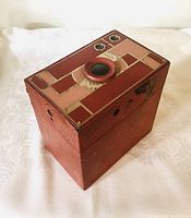 Front and angled view of the camera showing textured leatherette body and art deco top pattern with lens and two viewfinder windows.
