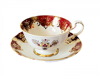 Side view of teacup and saucer showing red border with gold detailing and floral design