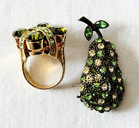 Photo showing the top and side view of the green rhinestone statement ring and pear brooch with overlapping perspective to highlight stones and metal color.