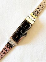 Metal link bracelet wristwatch with black rectangular dial, silver-tone case, and beveled glass crystal, photographed from angled top view on white background.