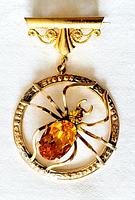 Front view of gold-tone Ward Brothers dangle brooch featuring insect bug with amber rhinestones within round frame and bar pin clasp.