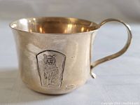 Full view of vintage child's cup showing side with embossed angry cat plaque and handle.