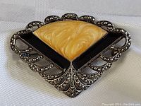 Close-up photo of the antique fan-shaped brooch pin showing the swirled creamy yellow center with surrounding black and marcasite encrusted metalwork.