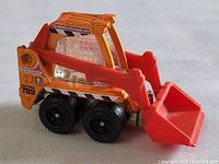 Side view of the Matchbox Bobcat Skidster toy showing the bright orange and red loader with black wheels and detailed stickers.