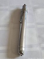 Full length view of the chrome precision medical flashlight showing smooth cylindrical shape, chrome clip, and push-button end cap.