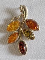 Close-up of the front of the silver pendant showing five amber stones of different colors and shapes, leaf motif.