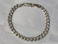 Full view of sterling silver thick link bracelet laid flat on fabric surface, showing clasp and thickness of links.