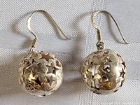 Close-up front view of one sterling silver spherical earring with star and heart cut-outs showing design details and hooks