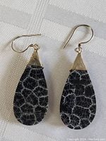 Close up photo of pair of dangle earrings with teardrop-shaped black stones with white spiderweb crackle pattern and simple sterling silver triangle tops with 925 mark and hook backs.