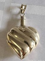 Front view of the heart-shaped sterling silver pendant perfume bottle showing ribbed design and top clasp for opening.