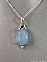 Close-up photo of blue chalcedony rectangular pendant set in silver-tone metal with small bead accents on top and bottom.