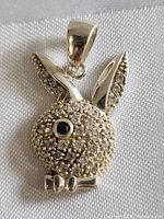 Front view of sterling silver Playboy Bunny pendant detailed with clear rhinestones and a black jeweled eye on a white fabric background.