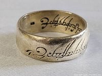 Close-up of sterling silver ring showing engraved script on outer surface and inner band.