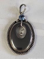 Front view of pendant showing oval black stone with twisted silver rope border and sapphire on top.