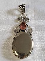 Full pendant showing the large smooth dark oval stone and the pink teardrop stone with intricate silver scroll details.