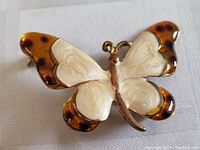 Butterfly enamel brooch pin front view showing white and amber enamel wings with gold-tone metal body and outlines.