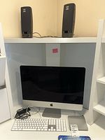 Shelf with two JBL speakers on top shelf; iMac front view with keyboard, cables, SuperDrive on lower shelf