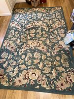 Full view of rectangular teal wool area rug with grapevine floral pattern laid on wood floor.