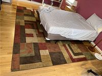 Full view of the area rug placed partially under a bed showing design and size.