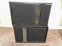 Front and top view of both Bose 301 speakers showing black fabric grille and vertical slat with Bose logo on one speaker.