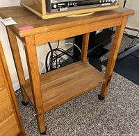 Wooden rolling cart from front showing top, legs, lower shelf, and casters.