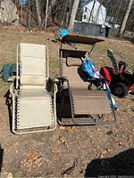 Image showing two lounge chairs side by side outdoors with a snow blower behind and umbrella folded on the brown chair.