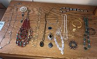 Full overview of costume jewelry lot displayed on wooden surface including necklaces, pins, pendants and earrings.