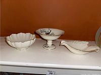 Three Lenox dishes on shelf: scalloped bowl, Serenade pedestal dish, and leaf-shaped gold trimmed dish.
