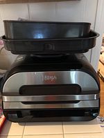 Front and side view of the Ninja Foodi Smart XL Grill FG550 with trays stacked on top.
