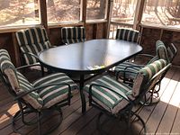 Wide view of the six patio chairs arranged around a rectangular glass-top table on a wood deck with wooded background; four chairs have swivel bases and two are stationary.