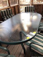 Oval glass patio table with green metal frame surrounded by four cushioned chairs featuring green and white striped fabric on porch.