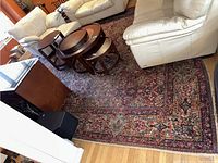 Full view of the Oriental style rug beneath white leather couches and round wooden nested side tables on a hardwood floor.