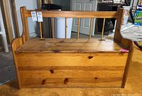 Front and side view of wooden storage bench showing spindle backrest, hinged top, wood grain, knots and wear on surface.