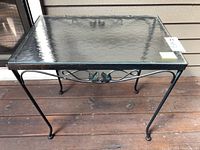 Front view of rectangular metal framed side table with textured glass top placed on wooden porch floor.