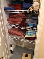 Full closet shelf showing towels and washcloths mainly in burnt orange, dark blue, and beige with a white digital scale at the bottom.