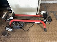 Side view of the log splitter on floor showing frame, cylinder, and wedge.