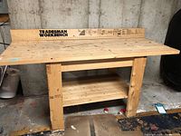 Front view of the wooden tradesman workbench showing the backboard with measurements and the sturdy legs and lower shelf.