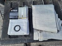 Two folded beige Eclipse Absolute Zero blackout curtains with metal grommets, original box included displaying measurement and features.