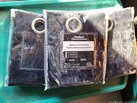 Three packages of brand new black blackout curtain panels with silver metal grommets visible through the packaging.