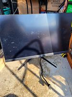 Front view of the Adorus gaming monitor showing the screen with some dust and smudges, on a V-shaped stand, with power cable extending from it.