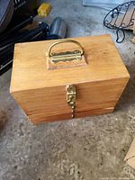 Closed wooden box with brass handle and latch, showing the exterior top and front.